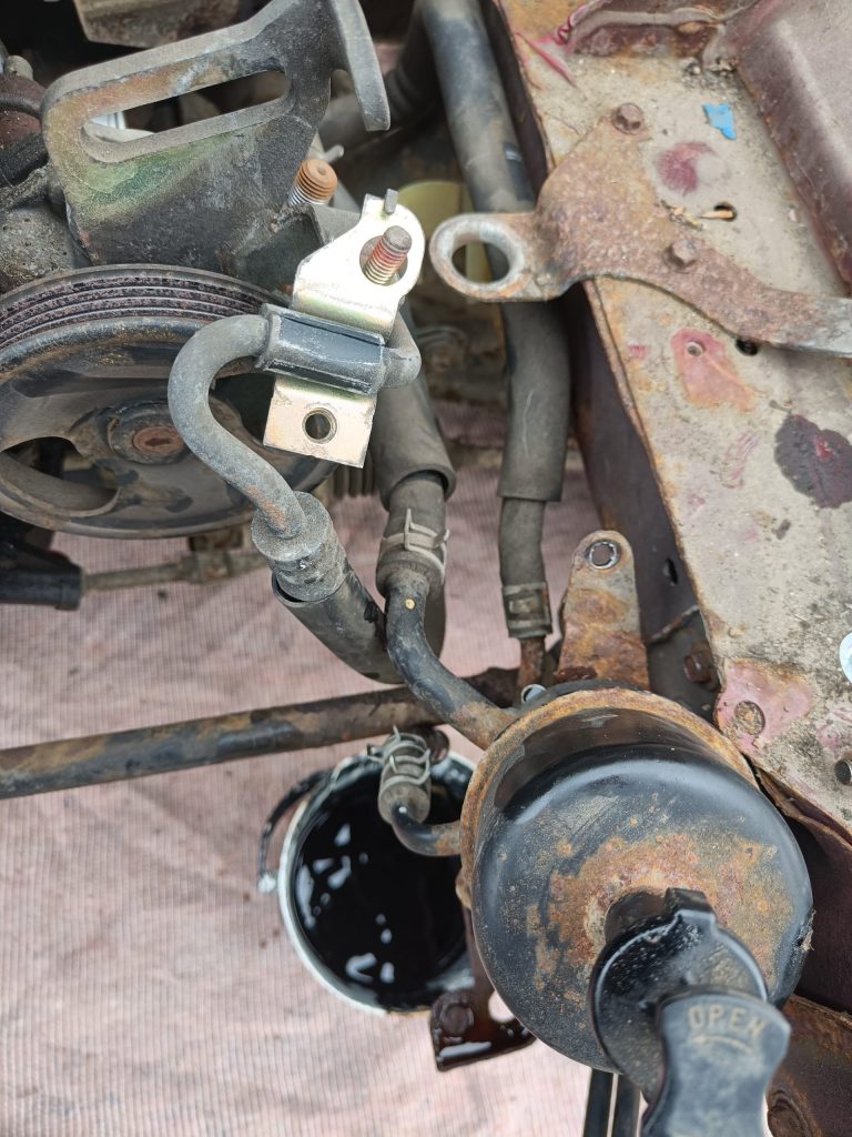 Image of unbolted power steering header tank draining into a bucket.