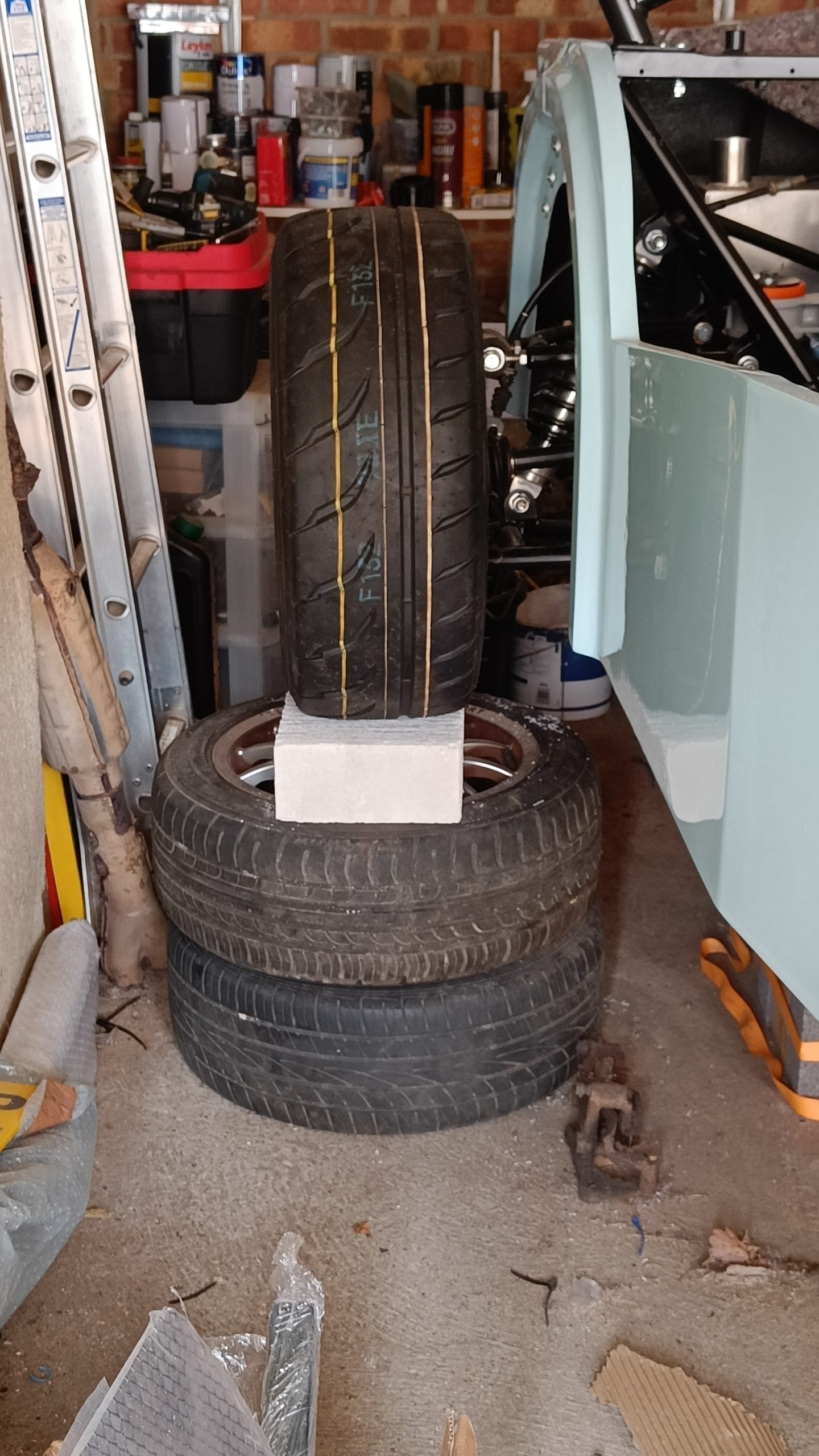 Image of rear of car being supported on OEM Mazda wheels and cement block!