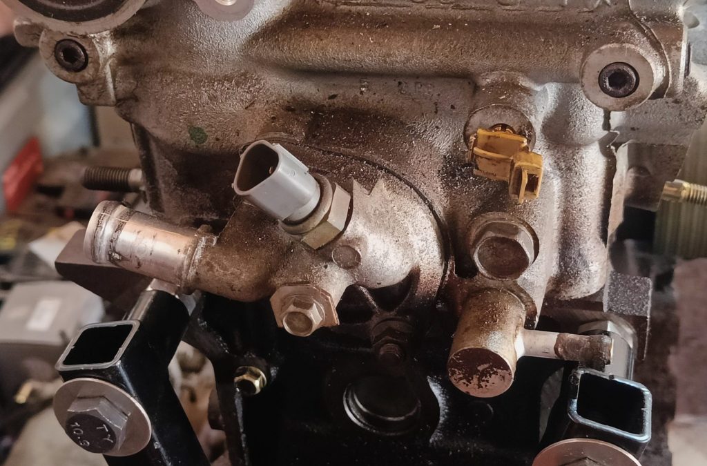 Image of rear of engine head showing water inlet and coolant temp gauge.